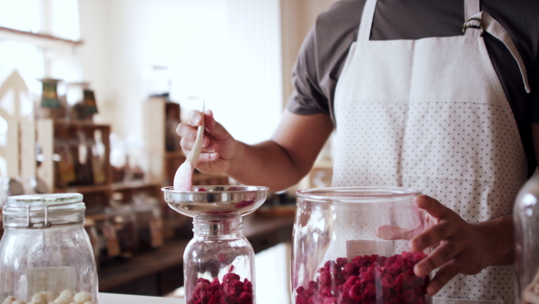 Unrecognizable young man filling jar by dryed raspberries in zero waste shop.