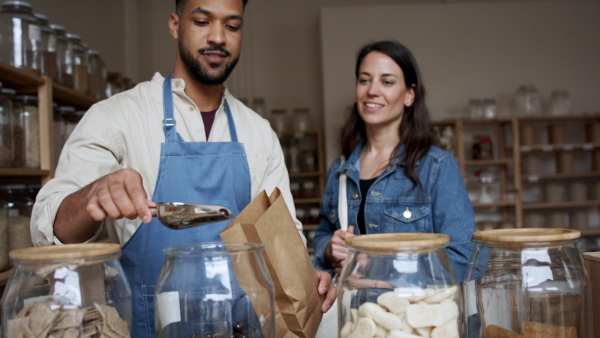 Young woman buying almonds in chocolate in zero waste shop.