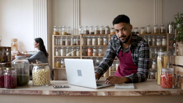 A fwner sitting in front of laptop and looking at camera in zero waste shop.