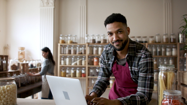 A fwner sitting in front of laptop and looking at camera in zero waste shop.