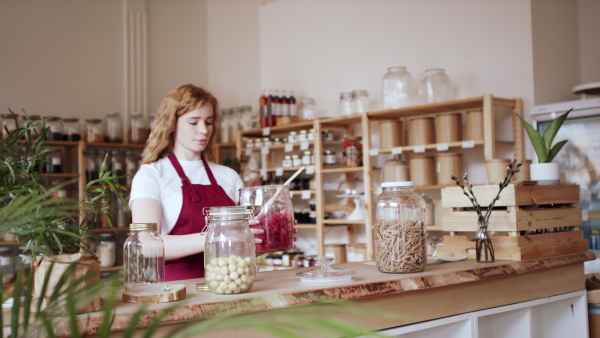 A young woman filling jar by dryed raspberries in zero waste shop.