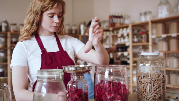 A young woman filling jar by dryed raspberries in zero waste shop.