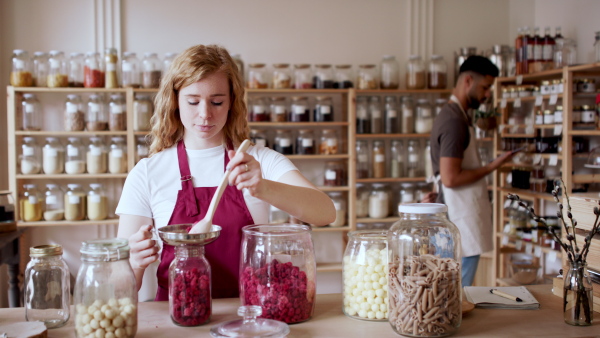 A young woman filling jar by dryed raspberries in zero waste shop.