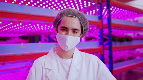 Front view of worker with face mask on aquaponic farm, looking at camera. Sustainable business and coronavirus.