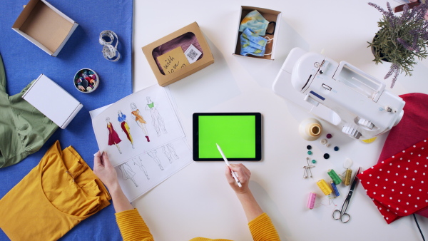 A top view of woman designing dresses on tablet with green screen, coronavirus desktop concept.