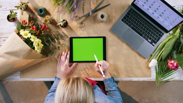 A top view of woman completing an order of flowers on tablet with green screen.