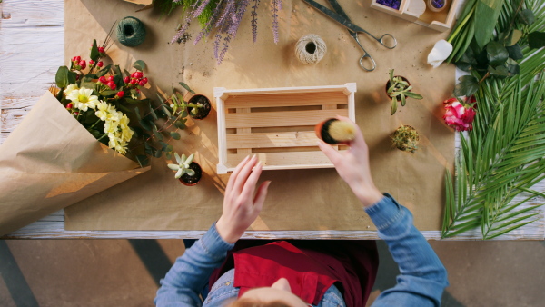 A top view of woman preparing an order of flowers into wooden box.