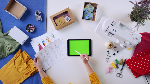 A top view of woman designing dresses on tablet with green screen, coronavirus desktop concept.