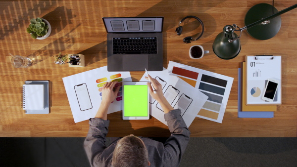 A top view of designer working on computer and tablet with green screen at desk in home office.