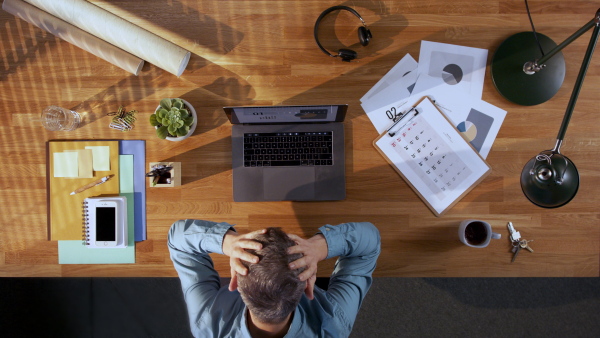 A top view of businessman working on computer at desk in home office, getting upset.