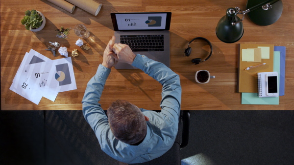 A top view of businessman working on computer at desk in home office, getting angry.