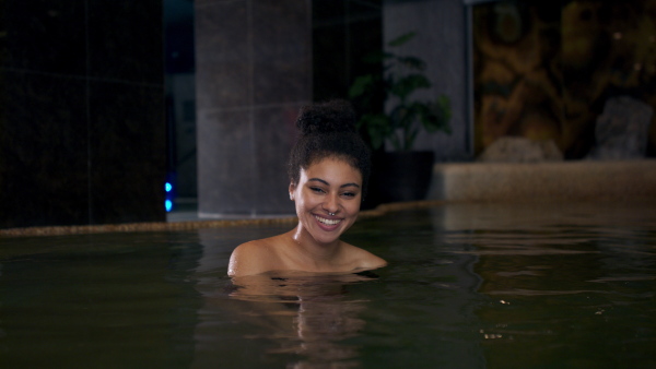 Portrait of happy young woman in indoor swimming pool, looking at camera.