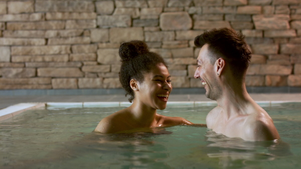 Happy young couple in indoor hot spring thermal pool, looking at camera.