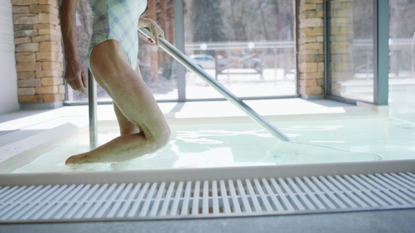 Senior woman walking in indoor swimming pool, healthy lifestyle concept.