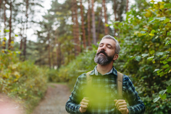 Handsome man standing in the middle of nature with closed eyes, enjoying peaceful atmosphere of forest, forestbathing.