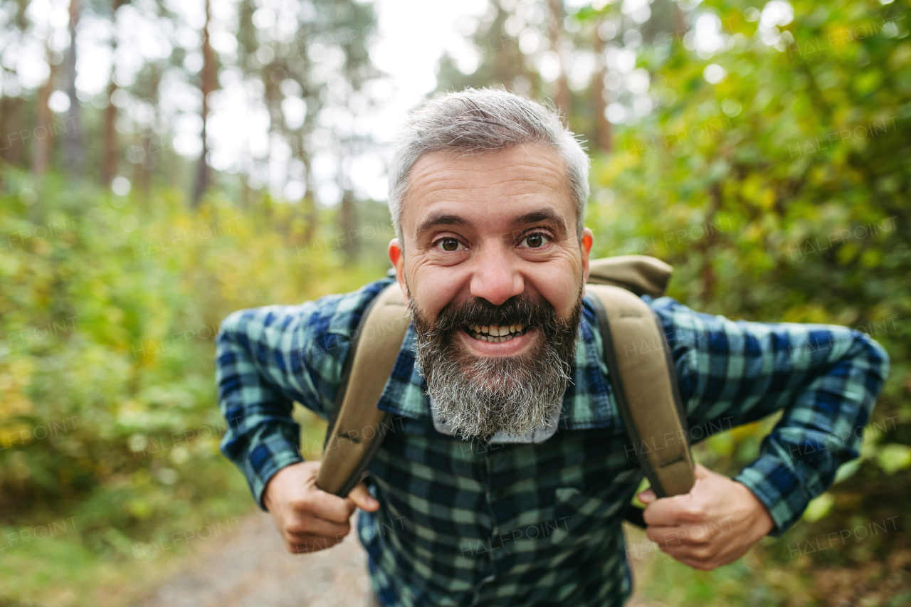 Smiling man standing in the middle of nature, looking at camera. Happy tourist with backpack.