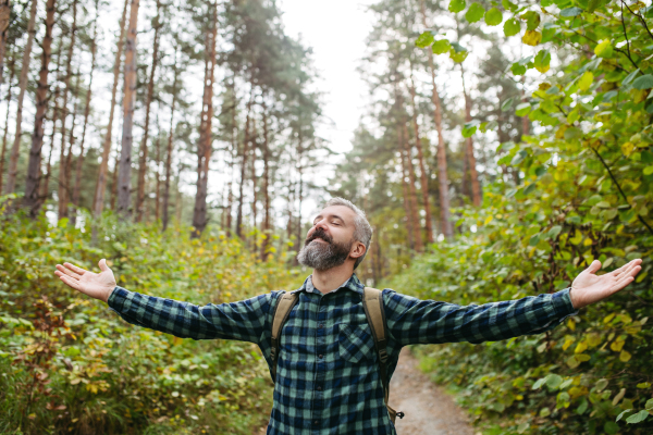 Man standing in the middle of nature with open arms and closed eyes. Peaceful atmosphere of the forest, forestbathing.