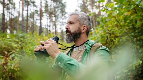 Tourist standing in the middle of nature, using binoculars to observe nature and wildlife inforest.