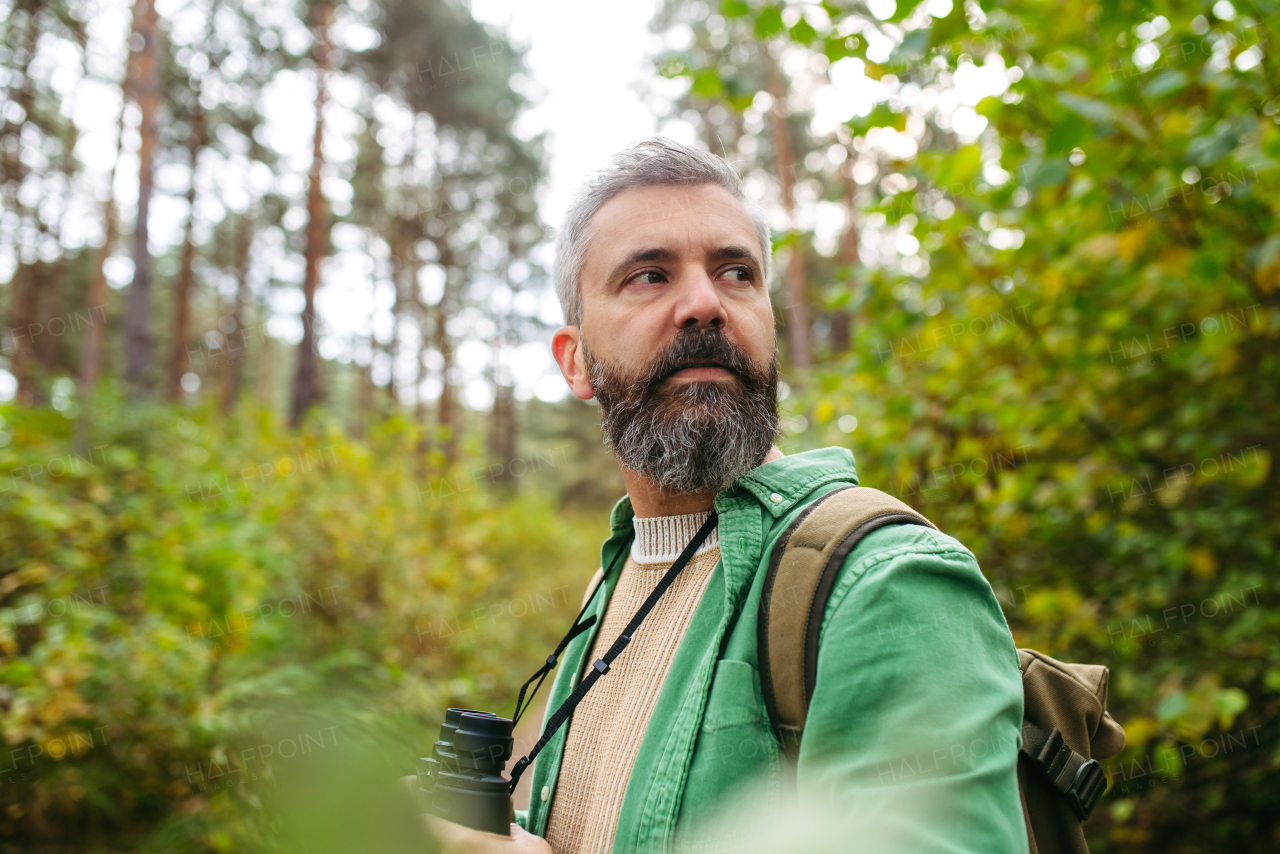 Handsome man watching wildlife with binoculars, enjoying peaceful atmosphere of forest, forestbathing.