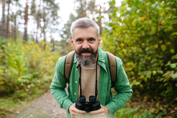 Man watching wildlife with binoculars, looking at camera and smiling. Birdwatching.