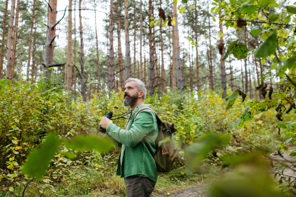 Tourist standing in the middle of nature, using binoculars to observe nature and wildlife inforest.