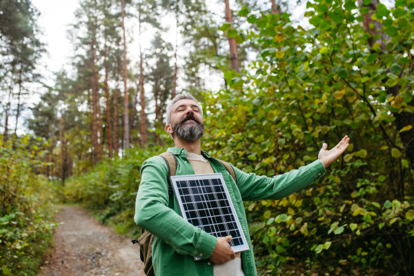 Handsome man standing in the middle of forest, holding small solar panel above his head