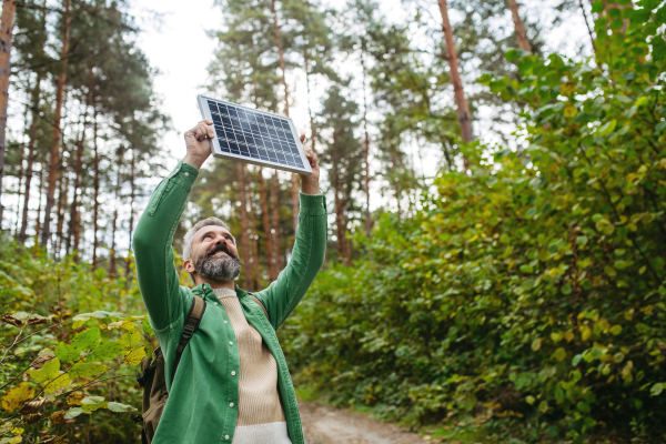 Handsome man standing in the middle of forest, holding small solar panel above his head