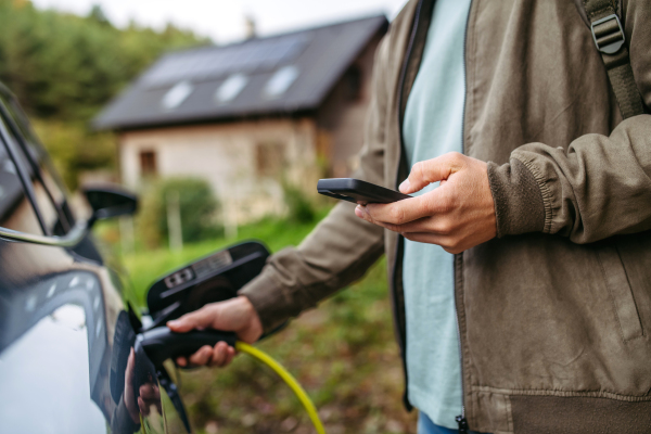 Portrait of a man charging his electric car in front of his house, plugging the charger into the charging port. The man is unplugging the charger from the fully charged car before going to the office.