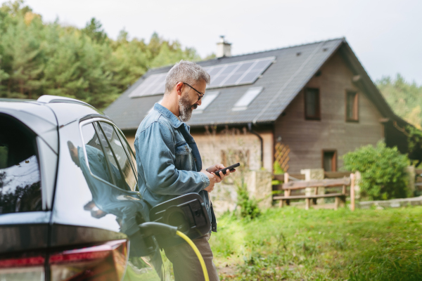 Portrait of a man charging his electric car in front of his house, plugging the charger into the charging port. The man is unplugging the charger from the fully charged car before going to the office.