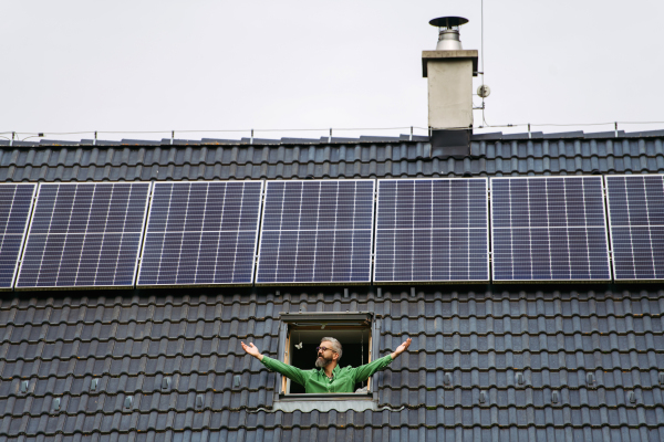 Man looking from skylight, roof window with solar panels above him. Sustainable lifestyle and green households