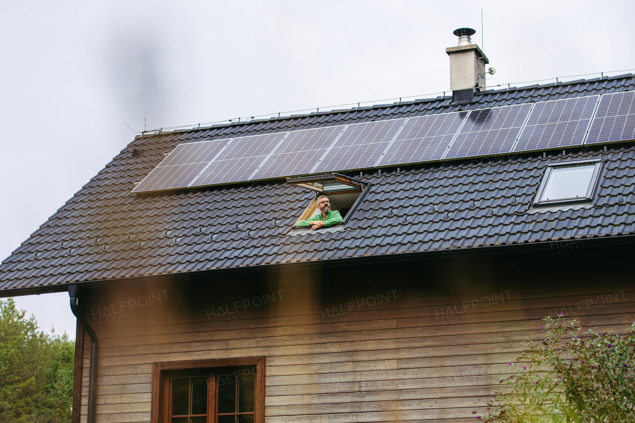 Man looking from skylight, roof window with solar panels above him. Sustainable lifestyle and green households