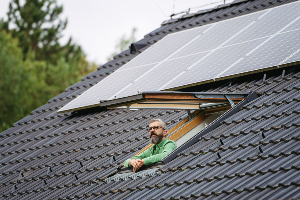 Man looking from skylight, roof window with solar panels above him. Sustainable lifestyle and green households