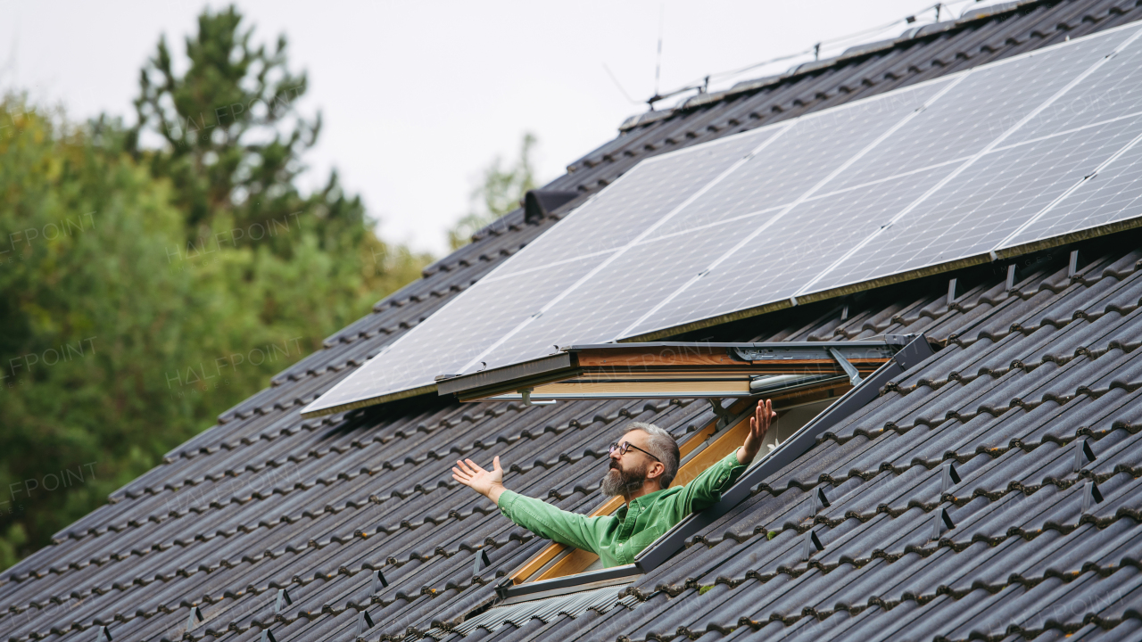 Man looking from skylight, roof window with solar panels above him. Sustainable lifestyle and green households