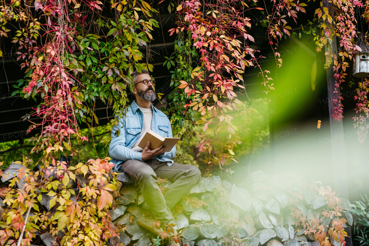 Man is enjoying relaxing, peaceful moment at home, sitting among greenery and reading a book.