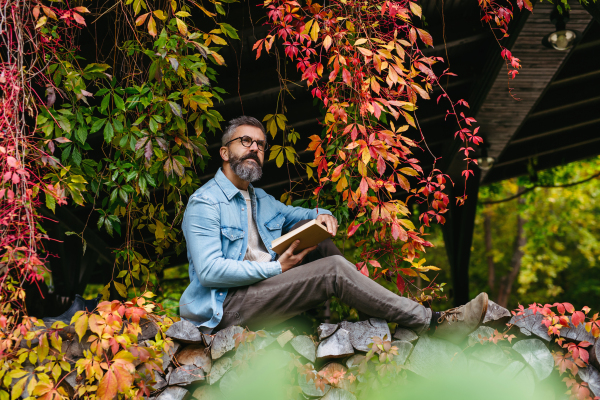 Man is enjoying relaxing, peaceful moment at home, sitting among greenery and reading a book.