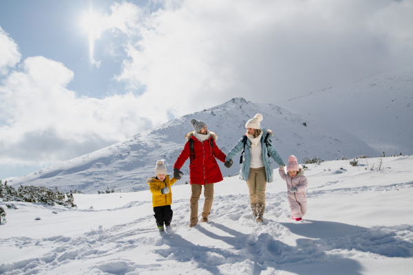 Family is enjoying winter holiday in the mountains, holding hands while walking through the snowy landscape.