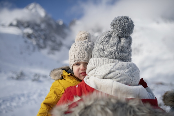 Father with tired small boy in the arms standing in the middle of snowy landscape, looking at winter mountains