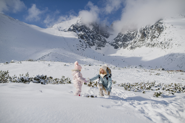 Mom playing with small girl. Family enjoying winter holiday in the mountains, playing in snow