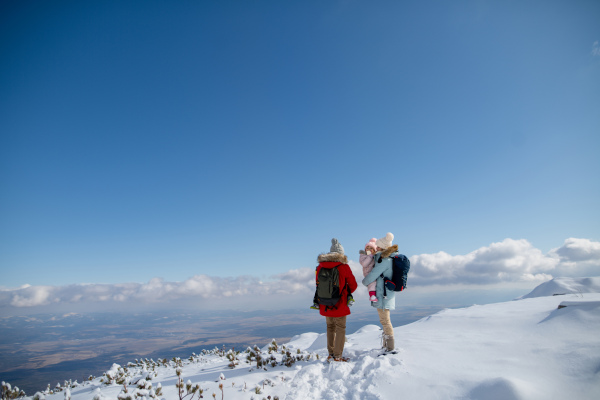 Parents with small kids standing in the middle of snowy landscape, looking at winter mountains and land under hill