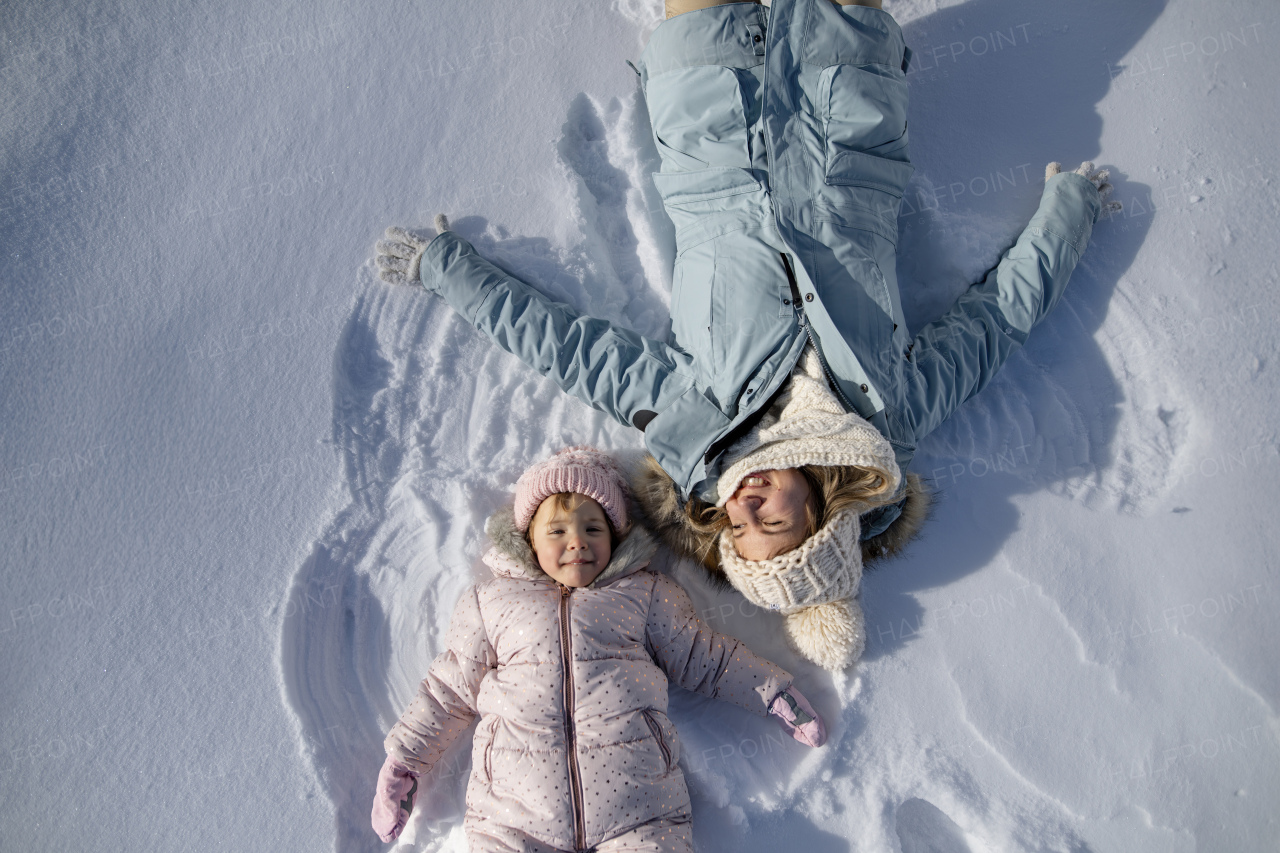 Portrait of small girl and mom making snow angels, enjoying winter holiday in the mountains.