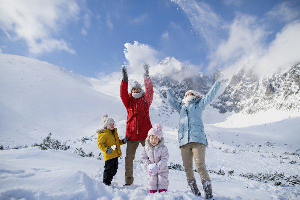 Family is enjoying winter holiday in the mountains, standing in the middle of snowy landscape, throwing snow in the air