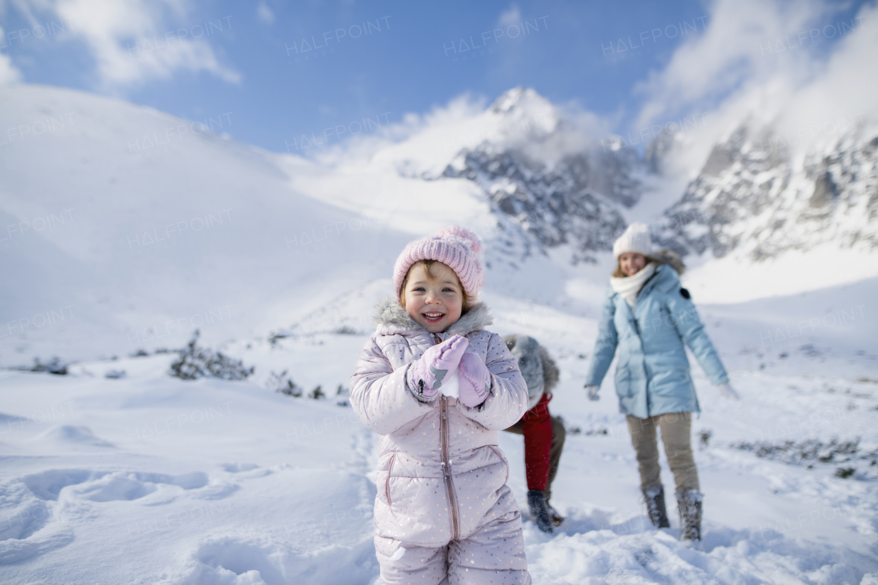 Portrait of a small girl enjoying winter holiday in the mountains with family, playing in snow, having snowball fight.