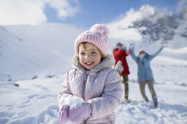 Portrait of a small girl enjoying winter holiday in the mountains with family, playing in snow, having snowball fight.