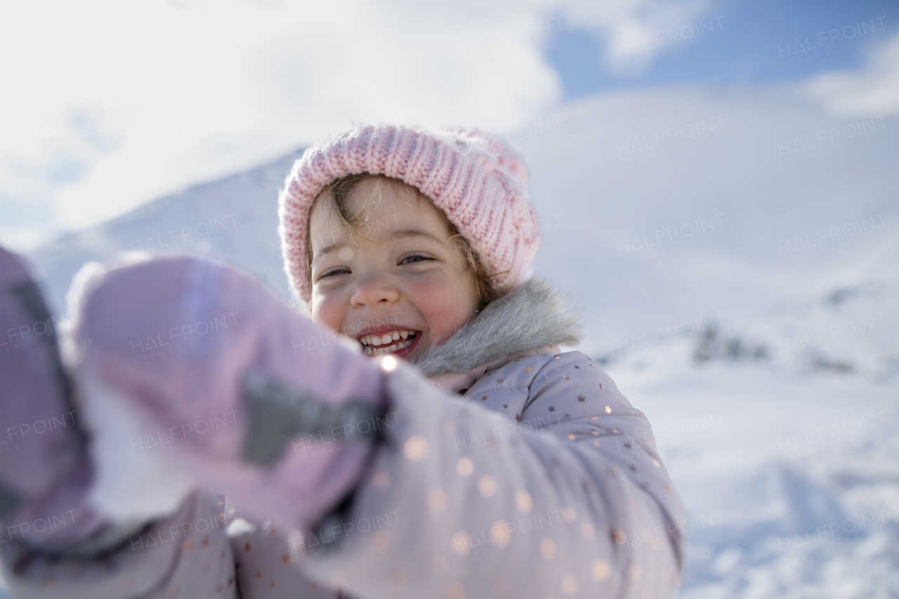 Portrait of a small girl enjoying winter holiday in the mountains with family, playing in snow.