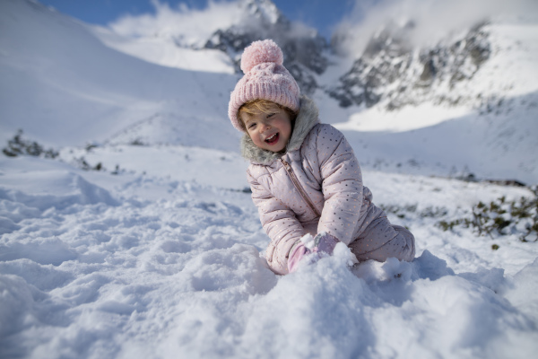 Portrait of a small girl enjoying winter holiday in the mountains with family, playing in snow.