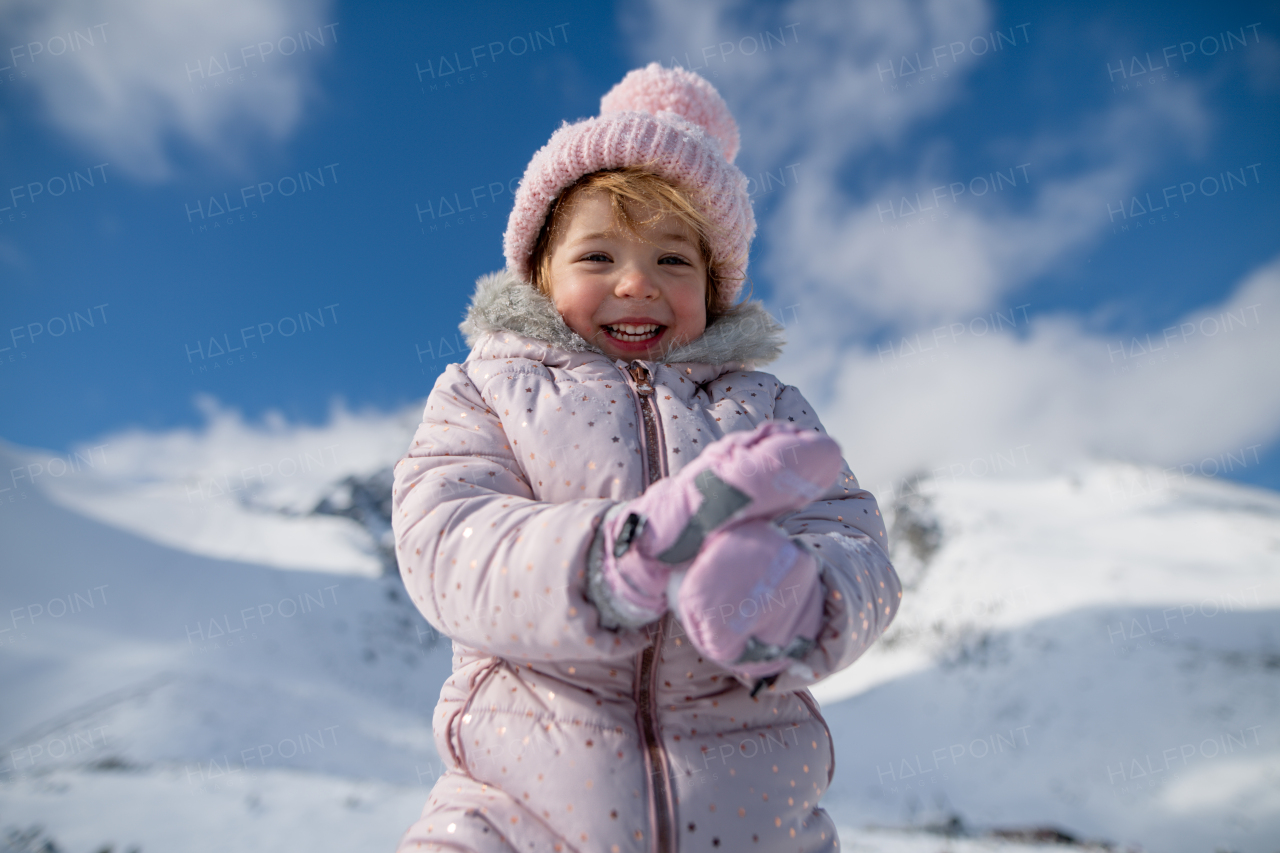 Portrait of a small girl enjoying winter holiday in the mountains with family, playing in snow.