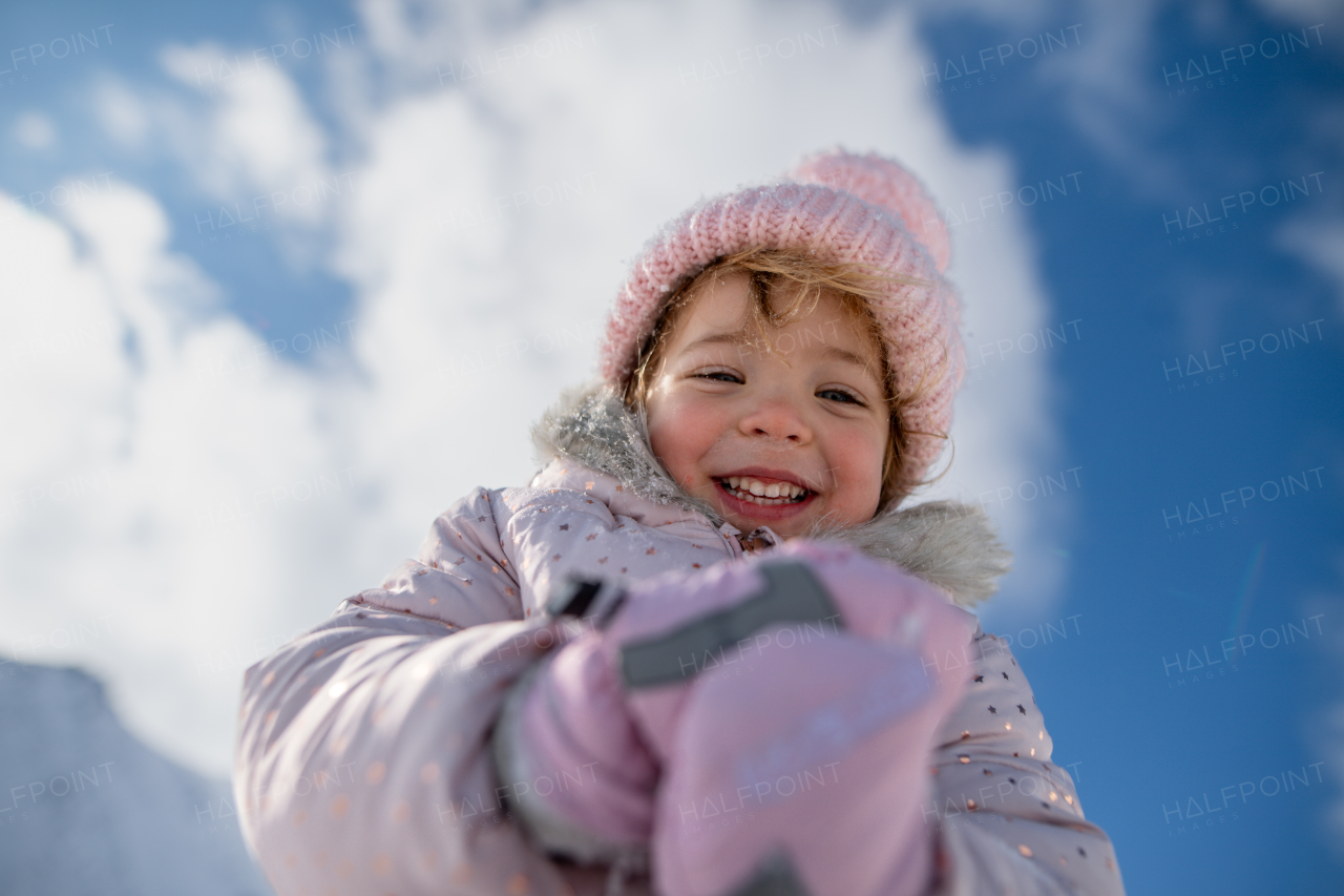 Portrait of a small girl enjoying winter holiday in the mountains with family, playing in snow.