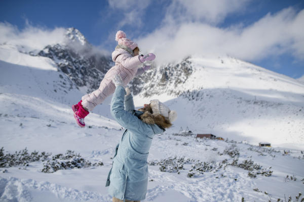 Mom playing with small girl. Family enjoying winter holiday in the mountains, playing in snow