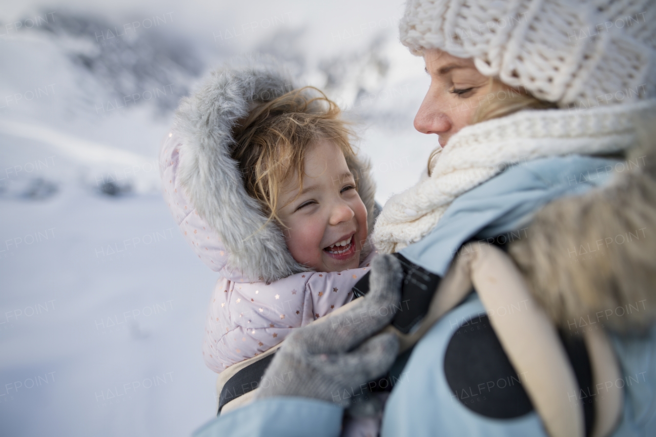 Mother standing in the middle of snowy landscape with daughter in baby carrier. Mom and girl enjoying winter holiday in mountains.