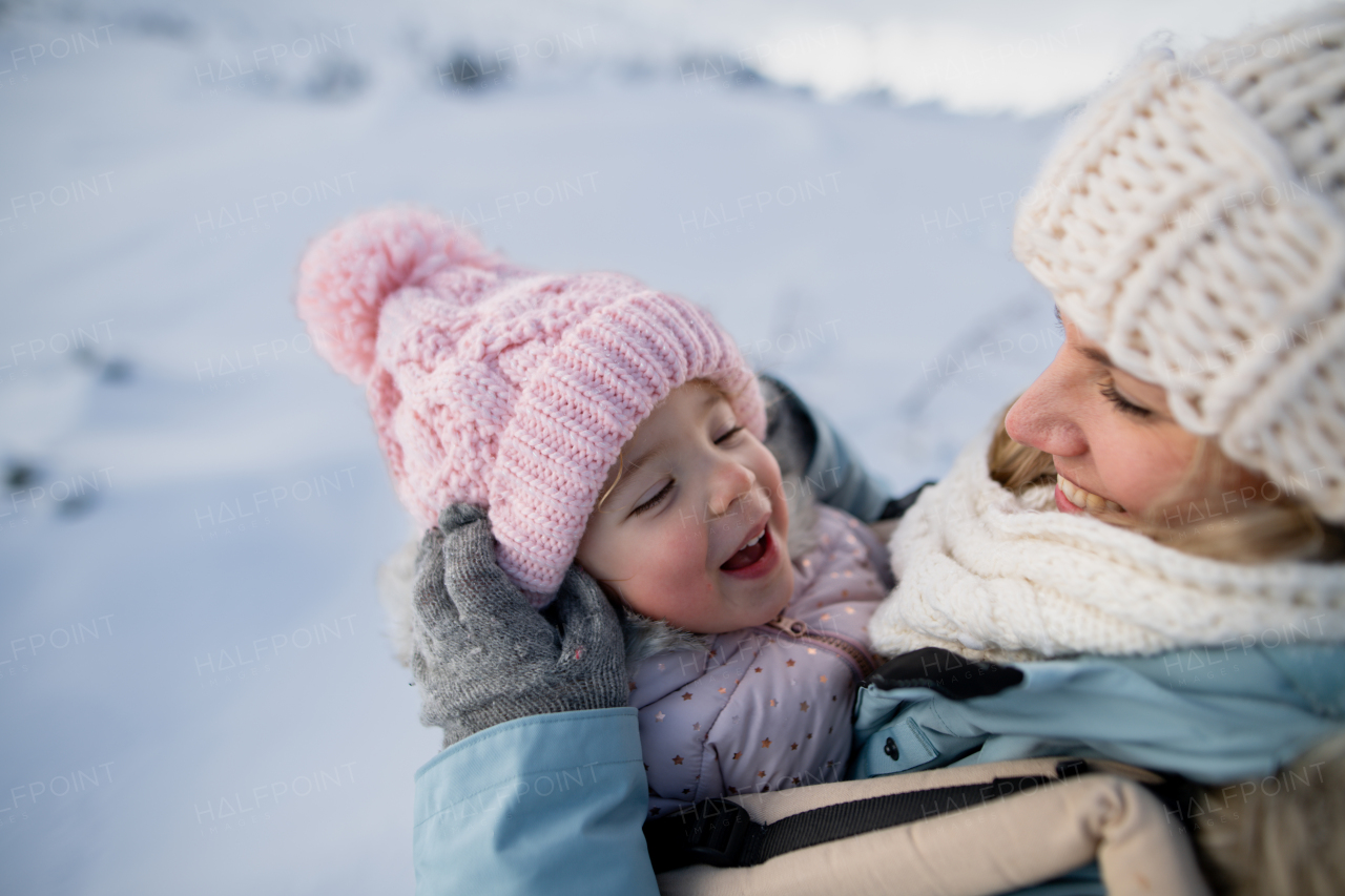 Mother standing in the middle of snowy landscape with daughter in baby carrier. Mom and girl enjoying winter holiday in mountains.